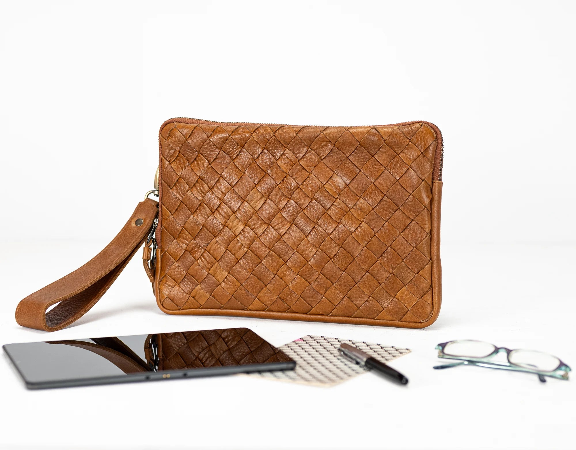 Brown woven clutch bag with phone, glasses, and pen on a white background