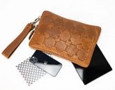 Brown leather clutch with honeycomb pattern, phone, and laptop on a white background