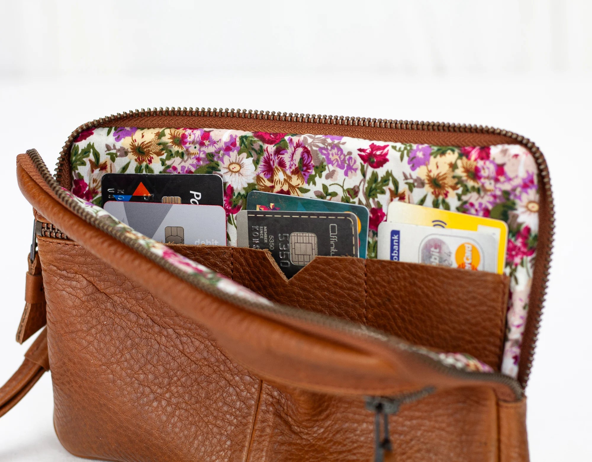 Brown leather handbag with floral lining containing various cards on a white background