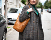 Woman in a plaid coat holding a brown woven bag on a city street.