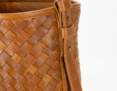 Close-up of a brown woven leather handbag with a strap on a white background
