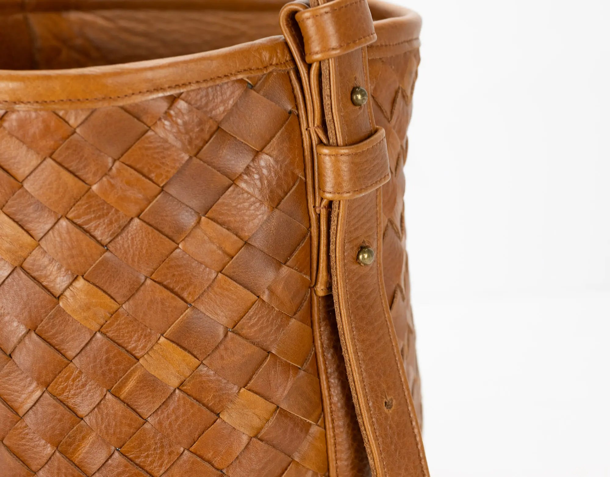 Close-up of a brown woven leather handbag with a strap on a white background