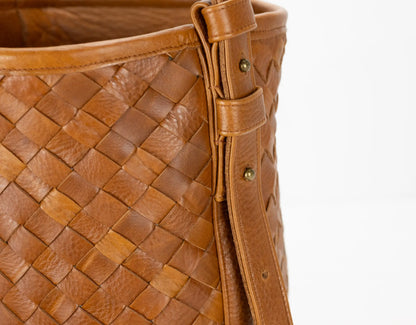Close-up of a brown woven leather handbag with a strap on a white background