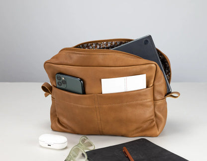 Brown leather bag with phone, notebook, and glasses on a light gray background