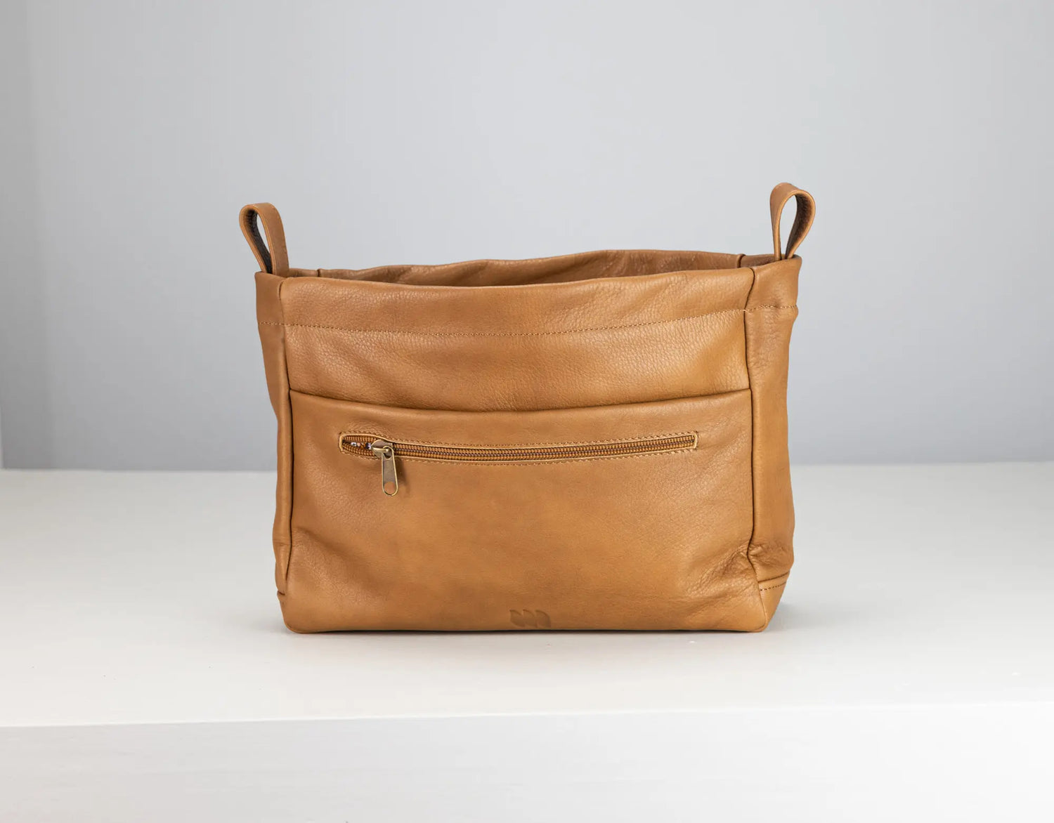 Brown leather bag with a zipper on a white surface and light gray background