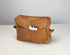 Brown leather toiletry bag with colorful markers on a light gray background