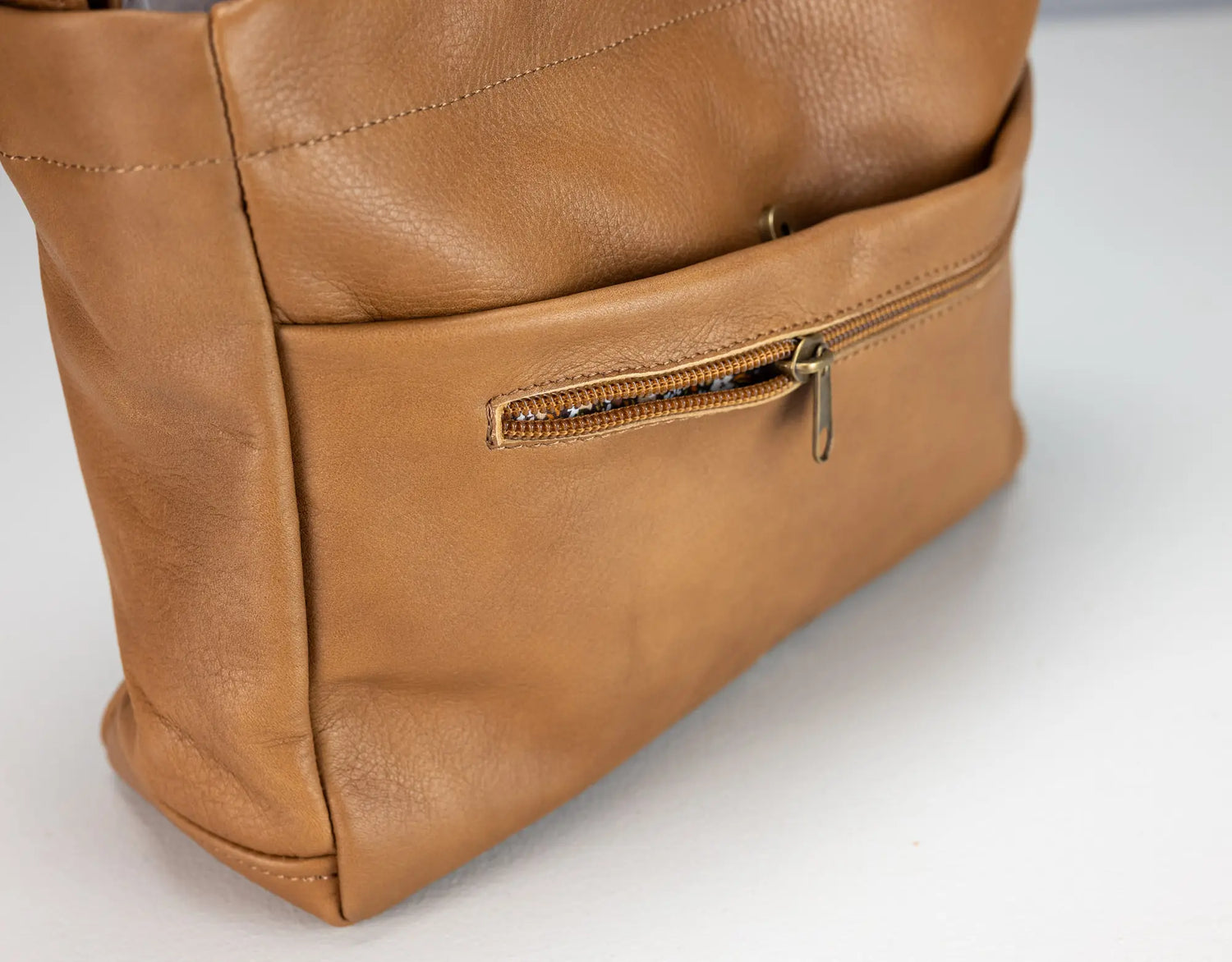 Close-up of a brown leather bag with a zipper on a white background