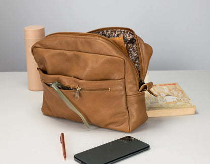 Brown leather bag with items like a phone and pen on a light surface.