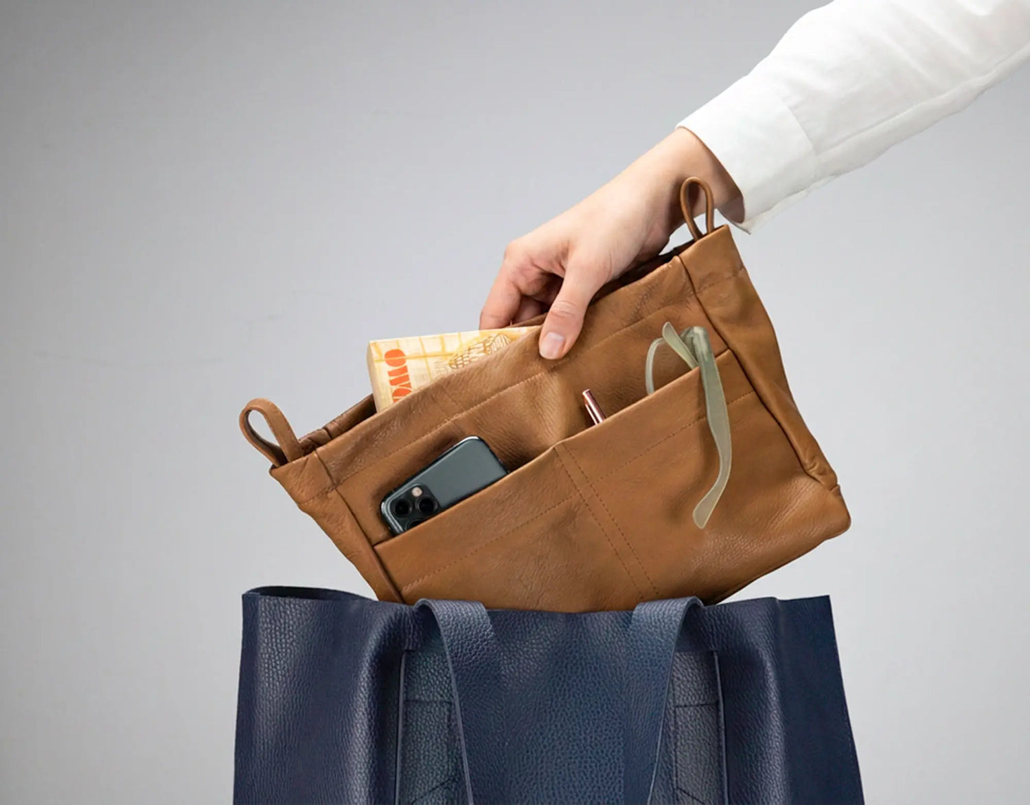 Brown leather pouch with phone and money held by a hand, against a gray background