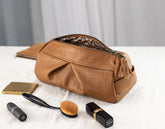 Brown leather toiletry bag with makeup items on a white surface