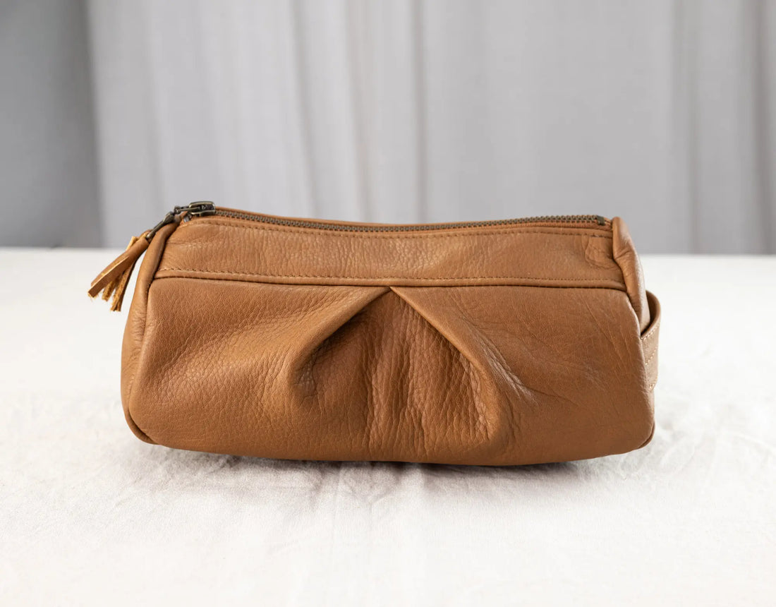 Brown leather pouch on a white surface with a gray curtain background