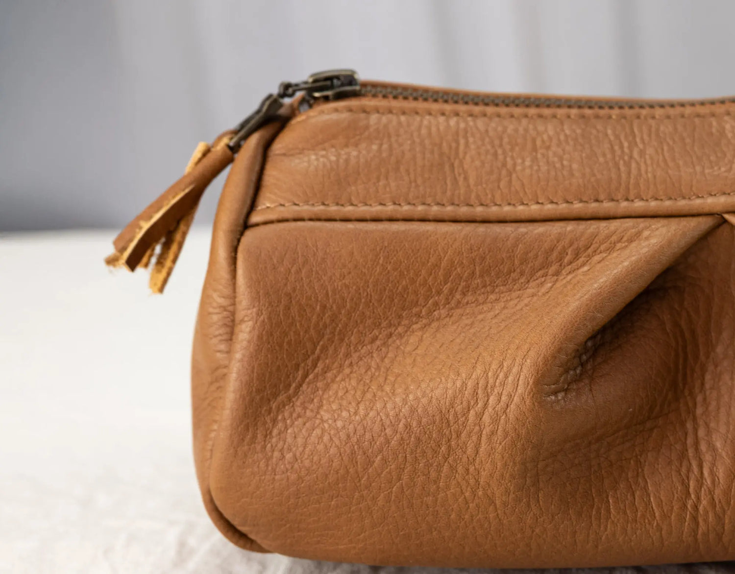 Brown leather clutch bag with a zipper on a light gray background