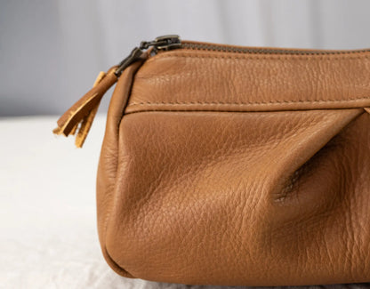 Brown leather clutch bag with a zipper on a light gray background