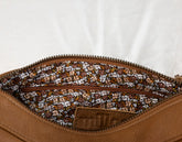 Close-up of a brown leather bag with floral patterned interior zipper on a white background
