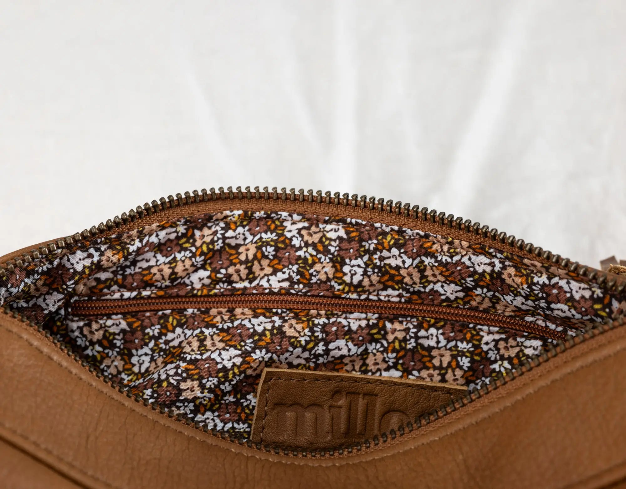 Close-up of a brown leather bag with floral patterned interior zipper on a white background