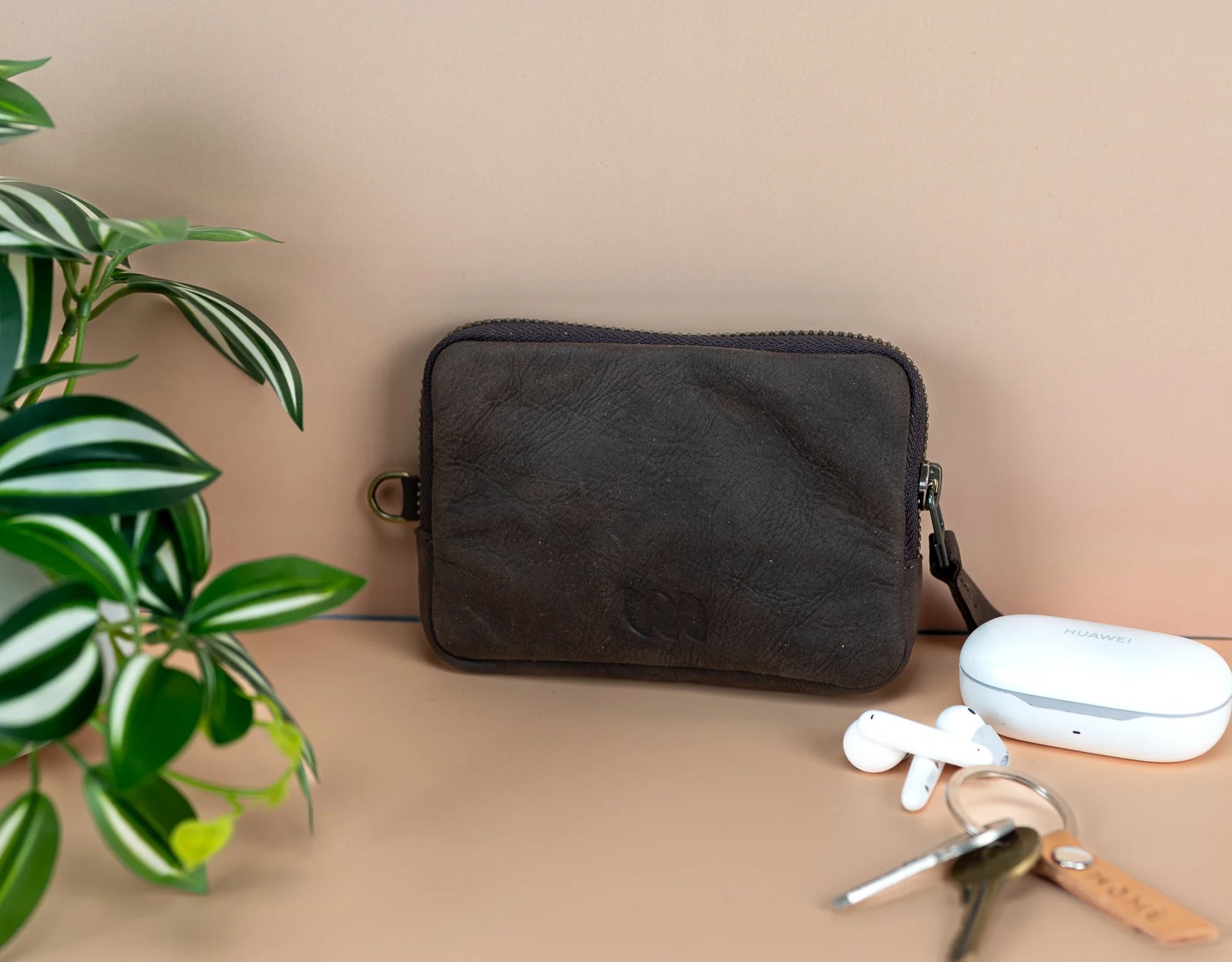Black pouch on a beige surface with a plant and keys in the background
