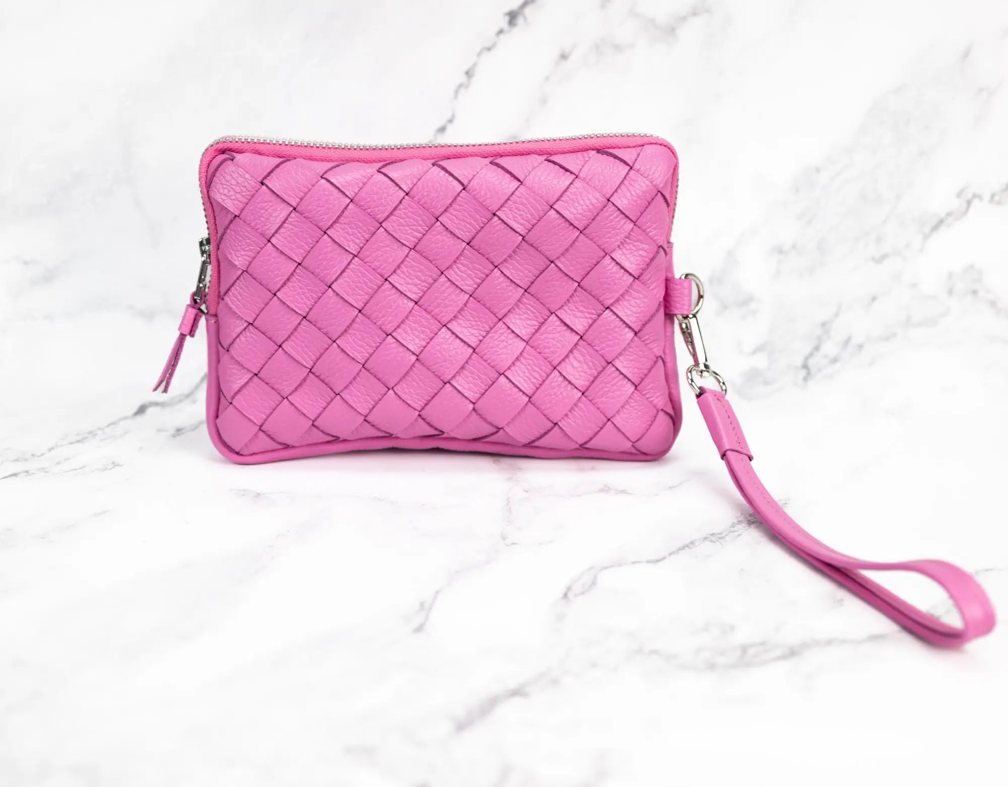 Pink woven clutch with a wrist strap on a white marble background