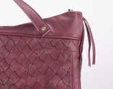 Close-up of a maroon woven leather handbag on a white background
