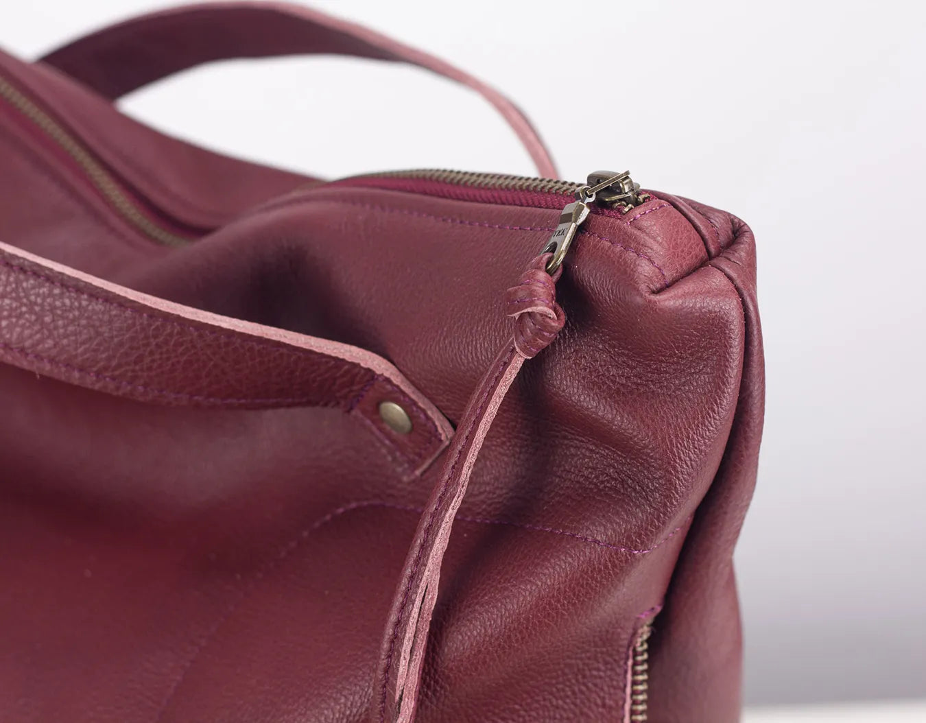 Close-up of a maroon leather handbag with a zipper on a white background
