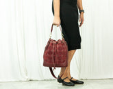 Person holding a red leather handbag against a white curtain background