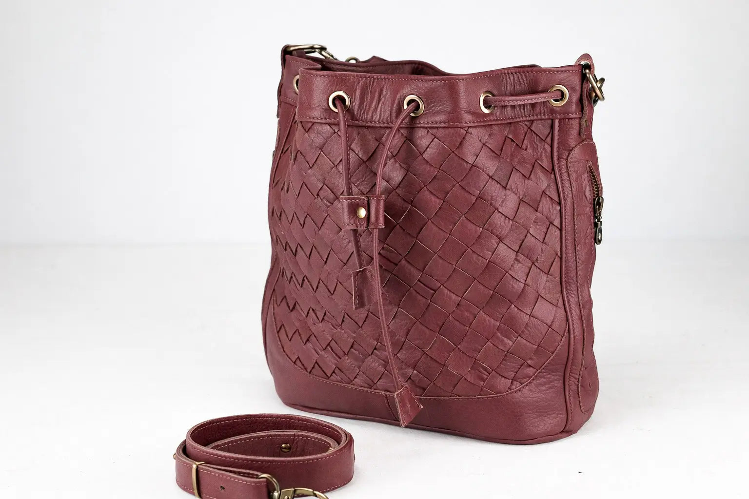 Maroon woven handbag with matching strap on a white background