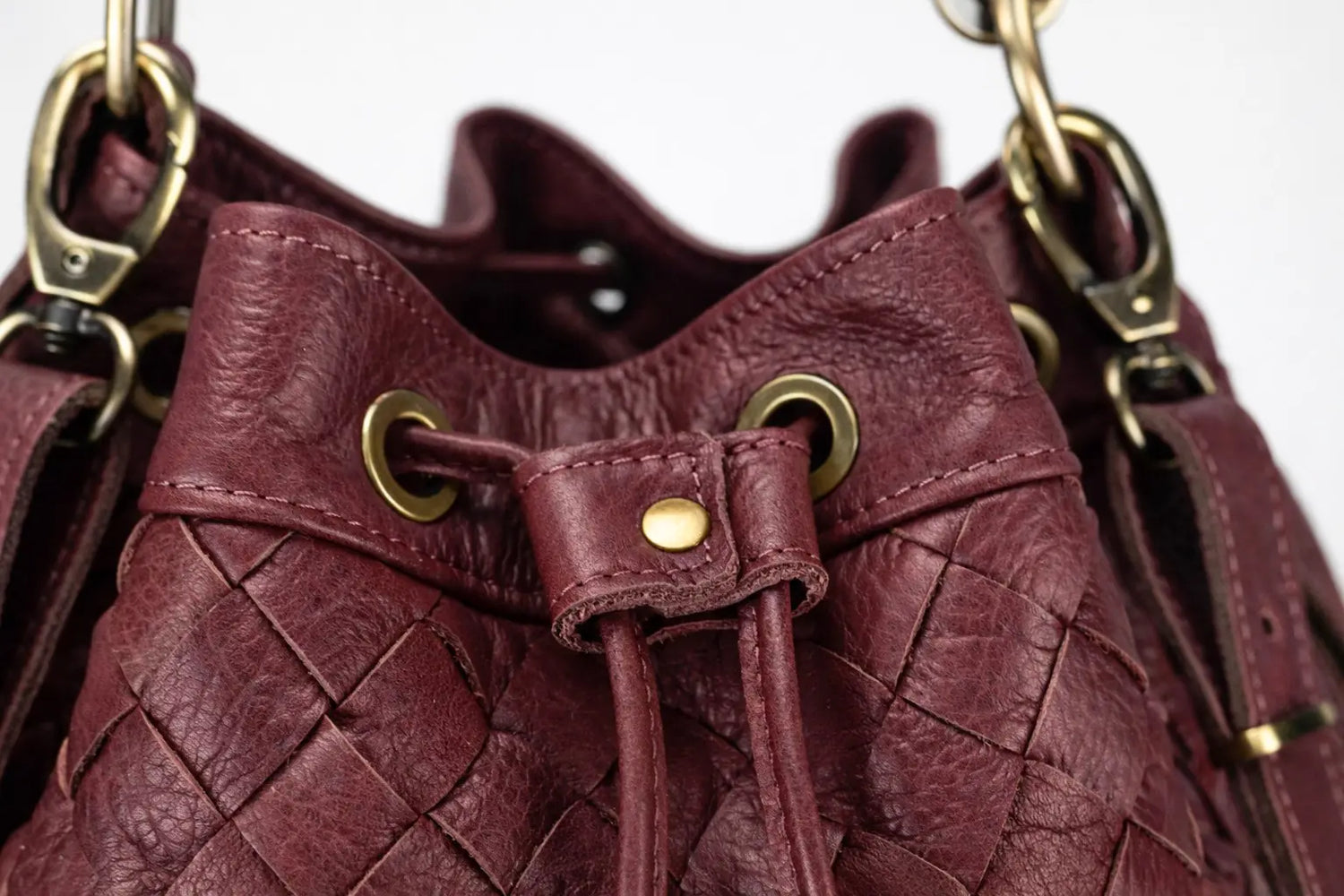 Close-up of a maroon leather handbag with gold hardware on a white background