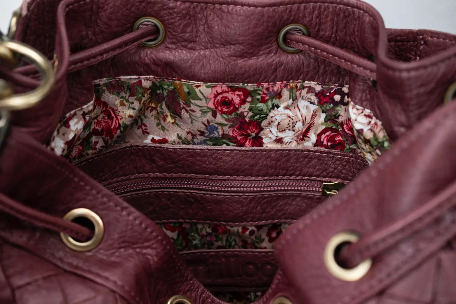 Close-up of a maroon leather handbag with floral interior lining.