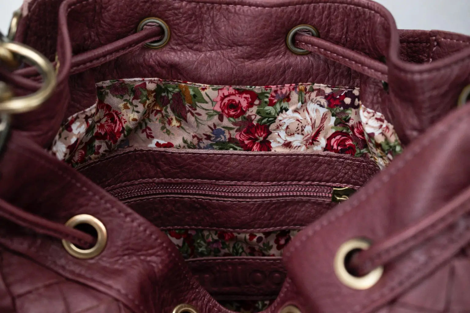 Close-up of a maroon leather handbag with floral interior lining.
