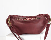 Maroon handbag with floral zipper pull on a white background