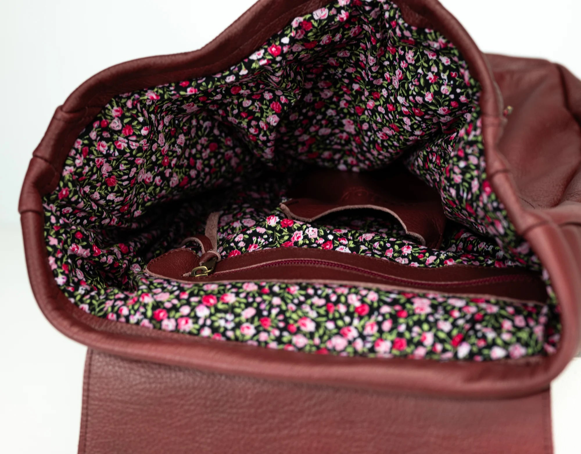 Brown leather handbag with floral interior lining on a white background