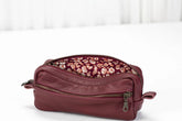 Maroon leather toiletry bag with floral patterned interior on a white background