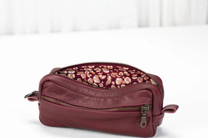 Maroon leather toiletry bag with floral patterned interior on a white background
