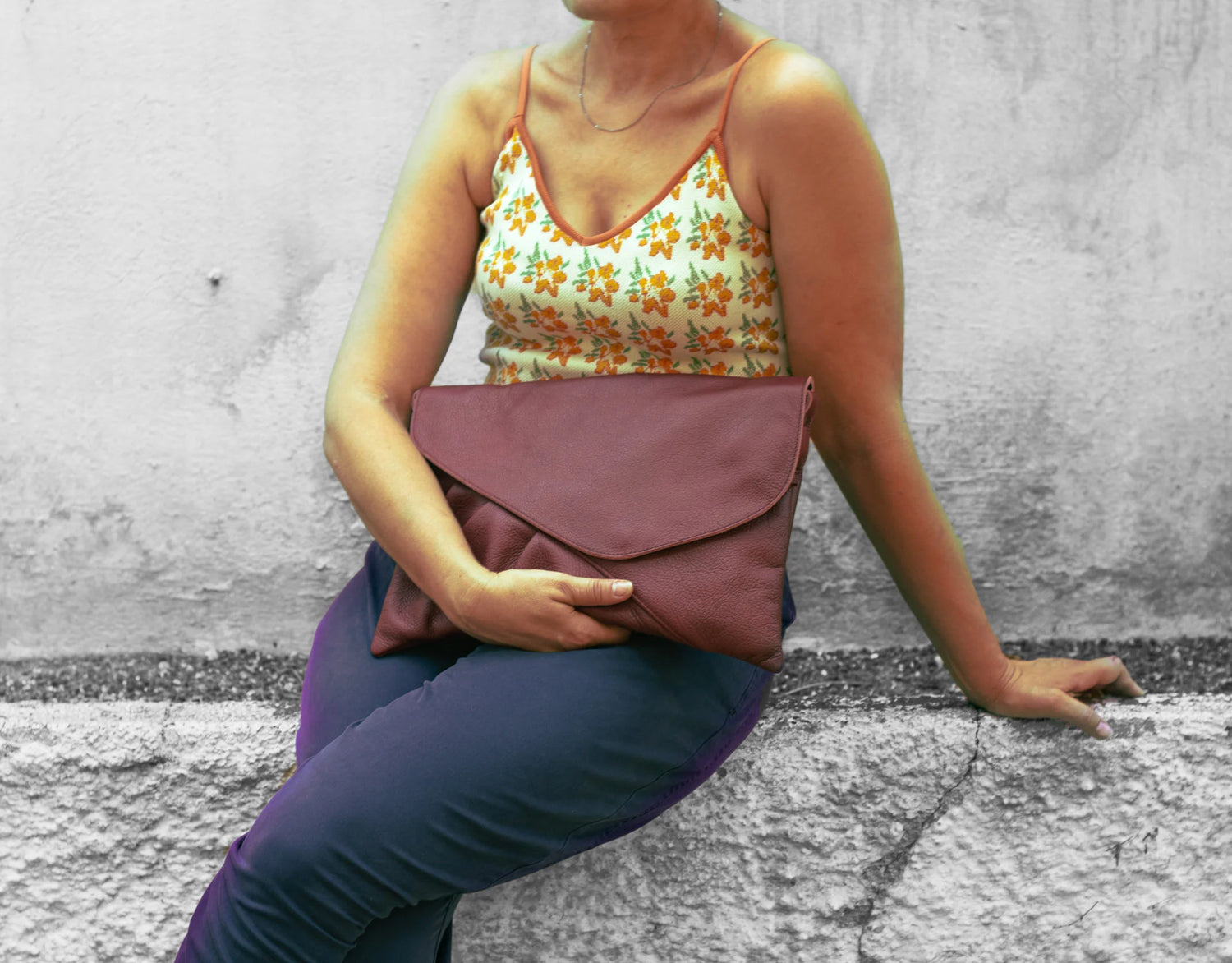 Person holding a maroon clutch bag against a textured wall background