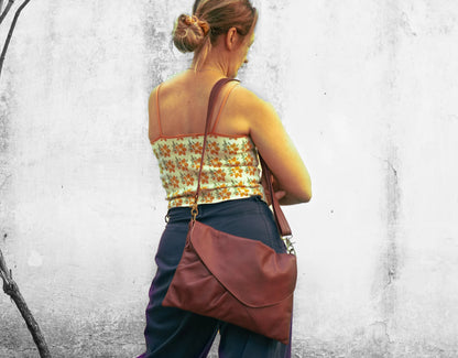 Woman carrying a burgundy leather bag against a textured white wall