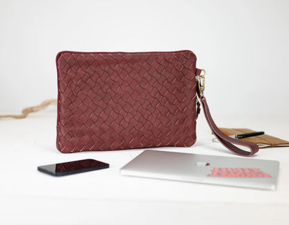 Red woven clutch bag on a white surface with a phone and laptop.