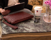 Maroon woven clutch on a marble table with a coffee cup and car keys.