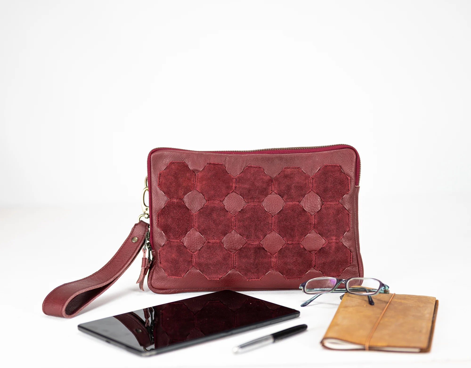 Red quilted clutch bag with phone, pen, and notebook on a white background