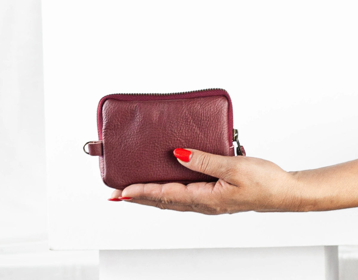 Hand holding a maroon leather wallet against a white background#color_burgundy