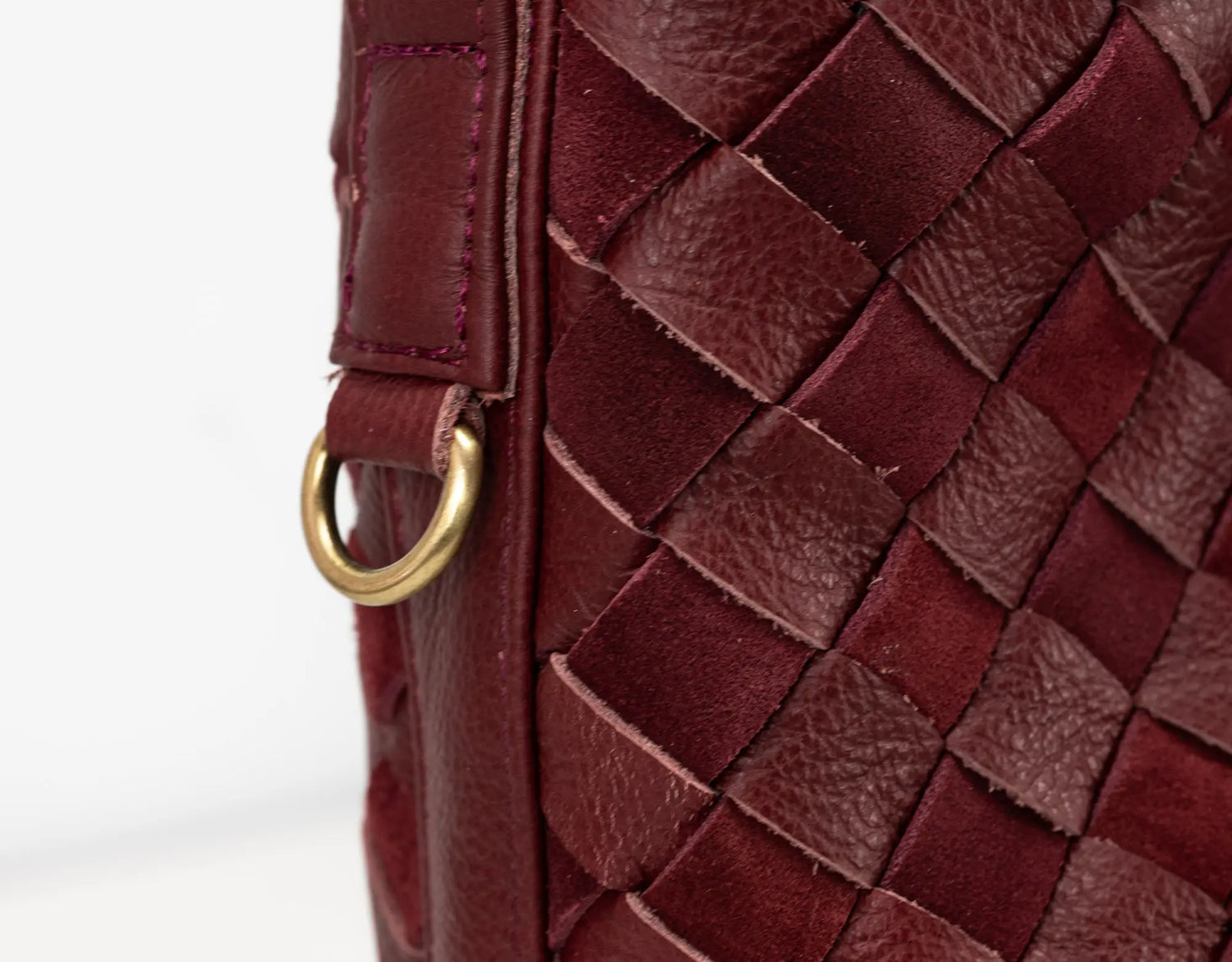 Close-up of a maroon woven leather handbag with a gold ring handle.