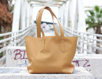 Caramel leather tote bag on a concrete surface with a blurred background