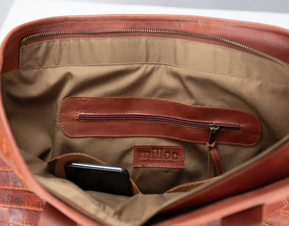 Close-up of the interior of a brown leather bag, showing a tan fabric lining, a zippered pocket, a phone in a pocket, and a small &