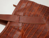 Close-up of a brown textured leather bag with a crocodile-embossed pattern and a matching leather strap detail on a white background.