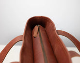 Close-up of the interior top opening of a brown leather bag, showing a zipper closure and part of the strap on a light gray background.