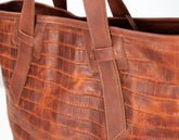 Close-up of a brown leather tote bag with an embossed crocodile pattern and matching leather handles.