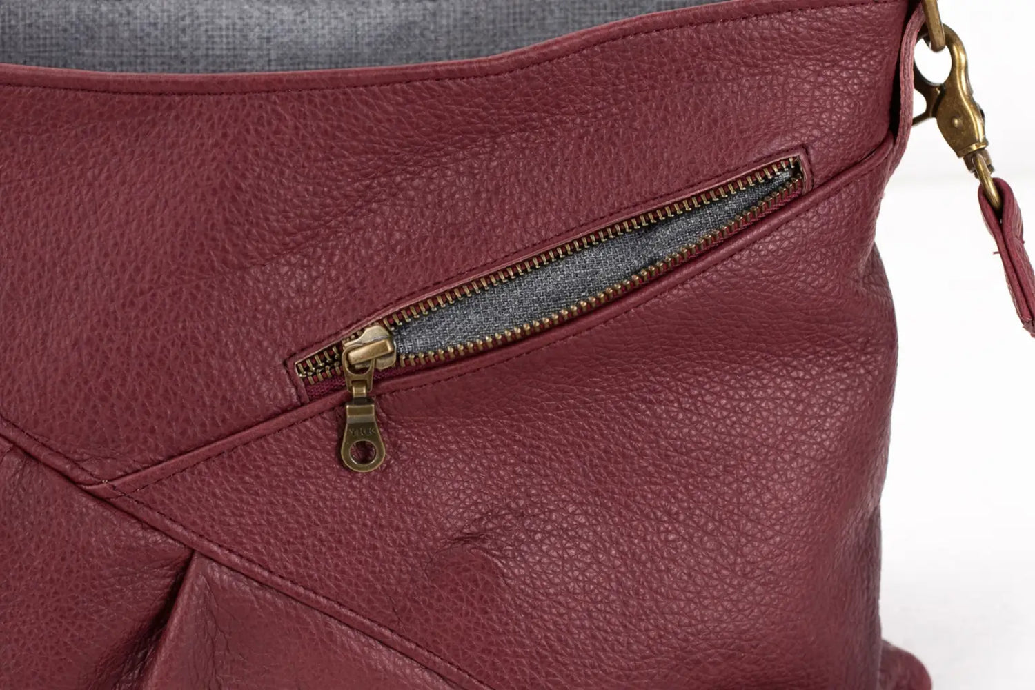 Close-up of a maroon leather bag with a gold zipper on a white background