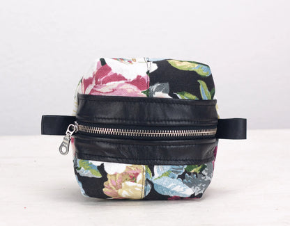 Floral-patterned bag with black leather accents on a white background
