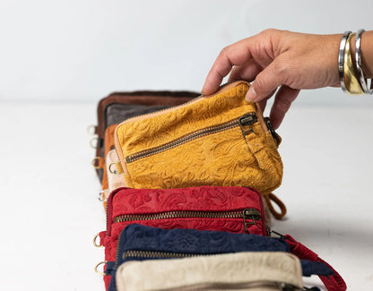 Stack of colorful leather wallets with a hand reaching to open one, on a light background