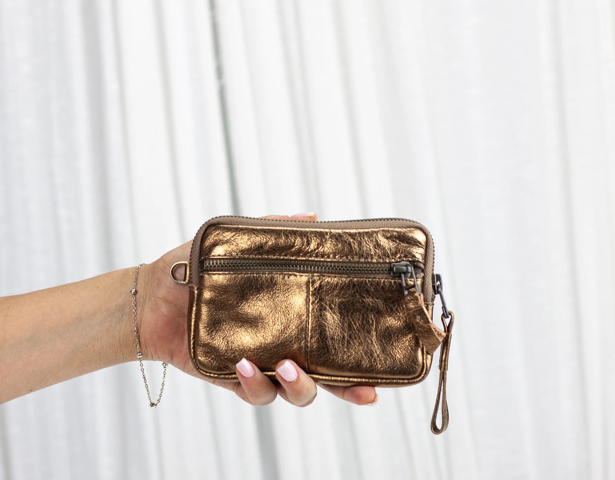 Gold metallic clutch held by a hand against a white background