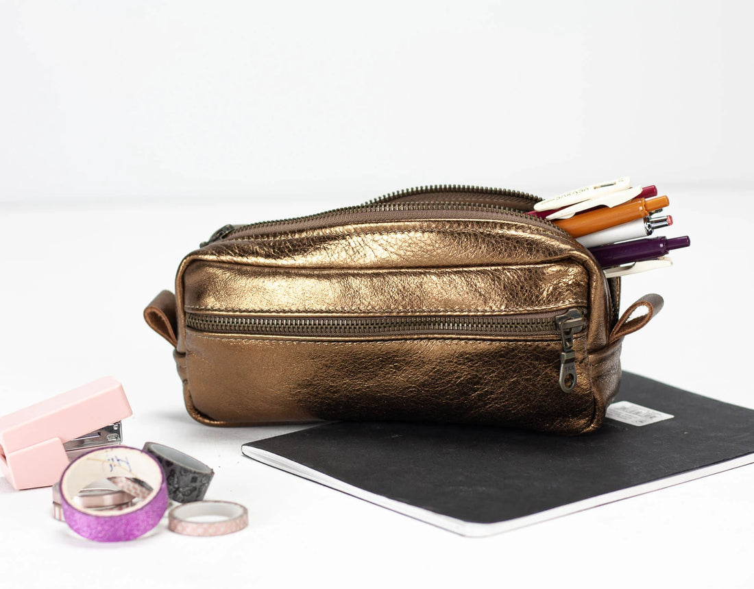 Brass metallic pencil case with stationery items on a white background