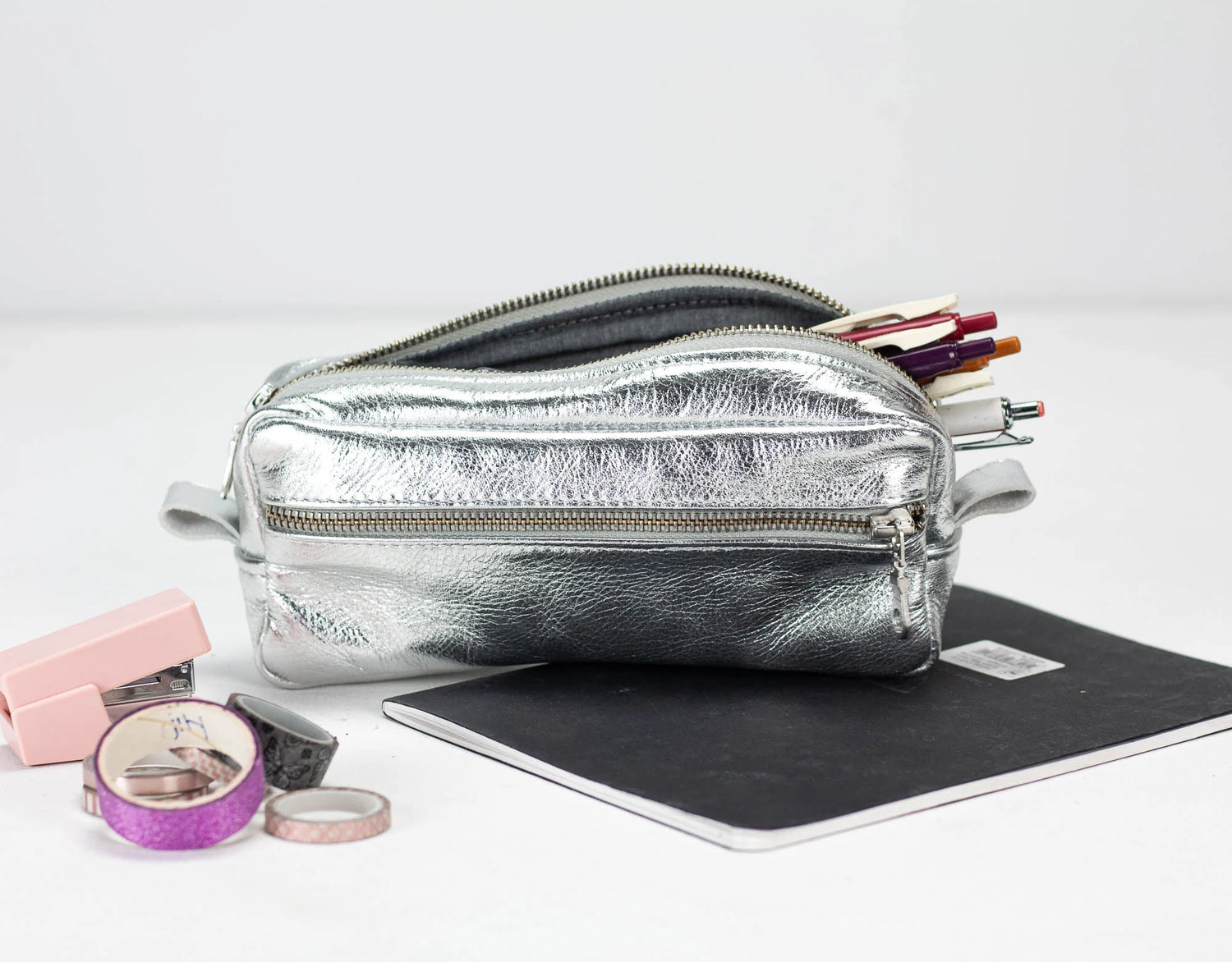 Silver pencil case with stationery items on a white background